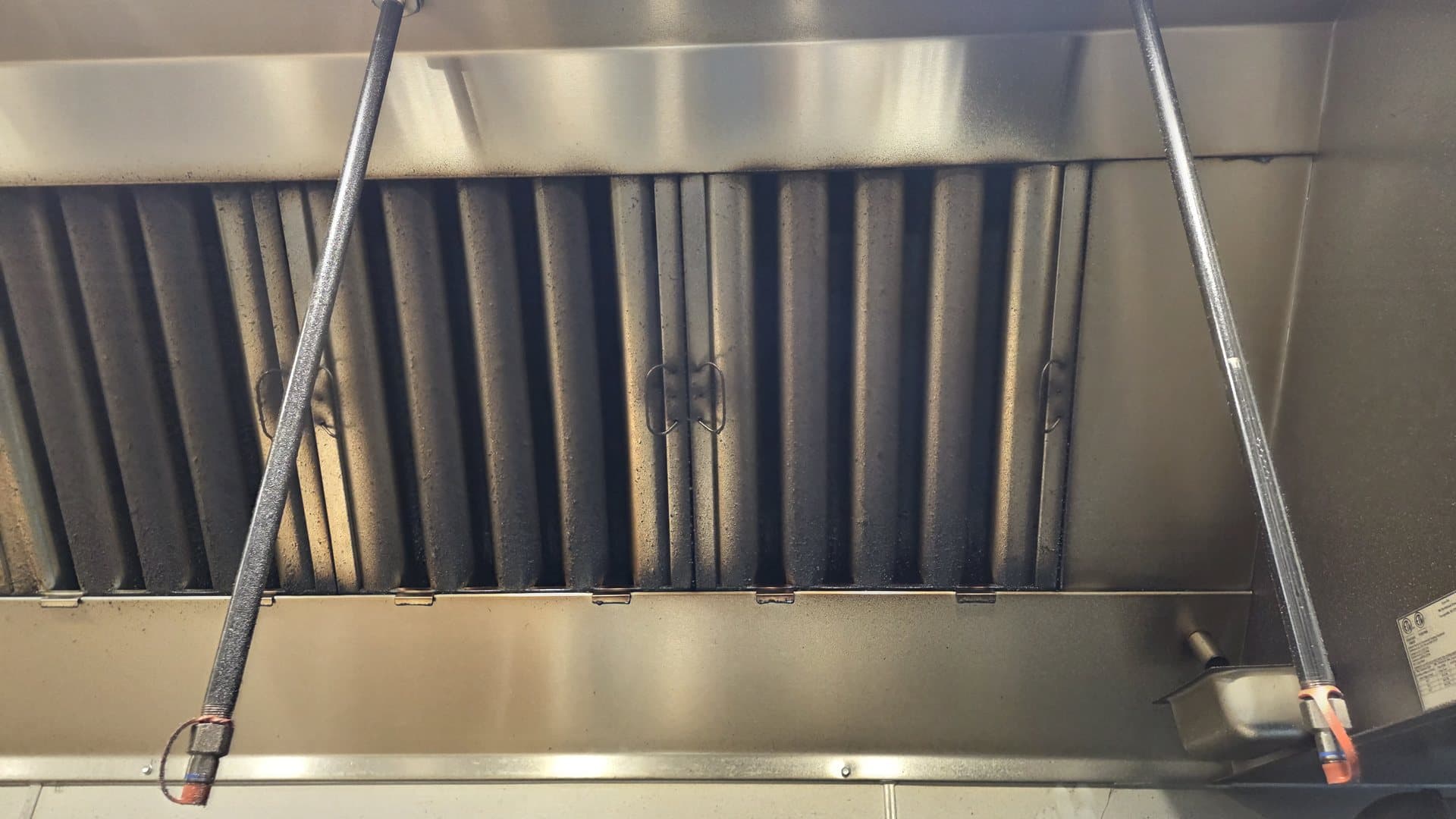 Grease-coated baffle filters in a kitchen hood, due for exchange, beside the grease cup at the end of the trough